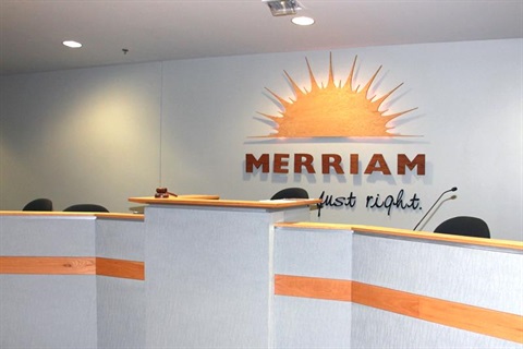 An empty Merriam City Council chambers with Merriam's logo of a sun and Merriam Just Right in background.