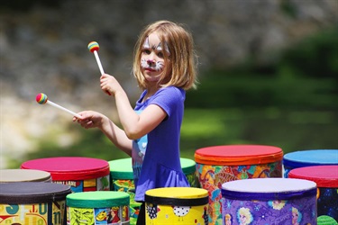 young girl with painted face banging drums