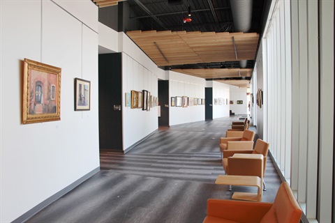 Gallery corridor featuring exhibited works on both walls and furniture down the right side