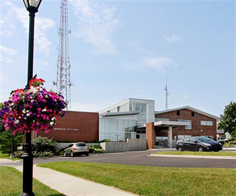 Merriam City Hall front entrance with hanging flower baskets in foreground. Building is red brick.