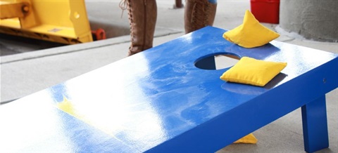 Blue cornhole board with two yellow bags perched on the edge of the opening