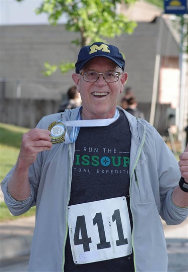 an older man proudly shows off his completion medal
