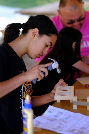 a young girl hard at work tapping a nail into a wood project