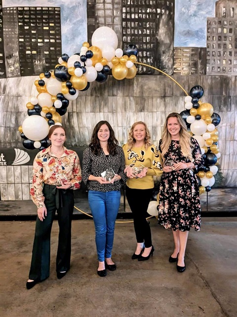 Four women and holding five awards. They're standing in front of a balloon arch.