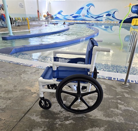 An aqua wheelchair on deck in front of the indoor pool at the MCC