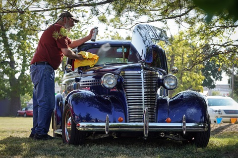 A man is cleaning his windshield on a classic car.