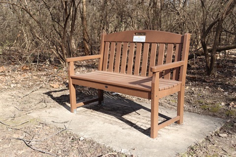 A brown plastic bench is perched on concrete along the Turkey Creek Streamway Trail.