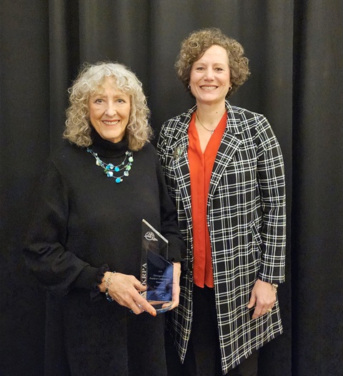 Two women are posing for a photo with Kathy Stull (on left) holding a blue and clear crystal award. 