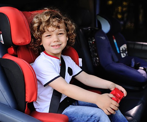 a young boy with curly hair in a booster seat in the back of the car