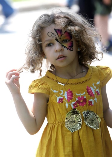 little girl with a painted butterfuly eye twirling her hair