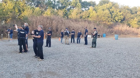 Officers are showing several academy members how to safely use a gun at on outdoor gun range.