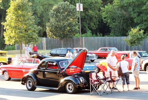 Hood up on a classic car while spectators chat with owner