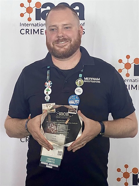 Seth Potts holds a crystal award in front of a logo backdrop.